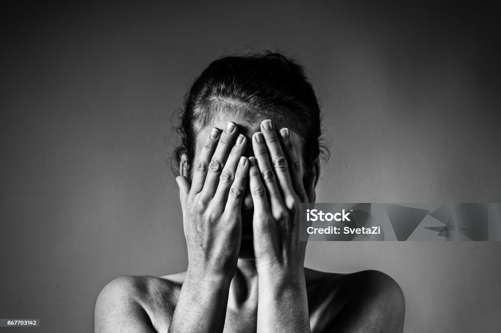 Concept of fear, shame, domestic violence. Concept of fear, shame, domestic violence. Woman covers her face her hands on light  scratched background. Black and white image. Women Stock Photo