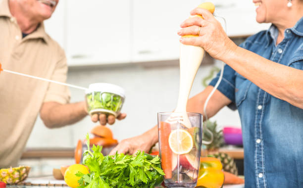 Senior couple having fun in kitchen with healthy food - Retired people cooking at home preparing blended centrifuge smoothie with bio fruit and vegetable - Happy elderly concept with mature pensioner Senior couple having fun in kitchen with healthy food - Retired people cooking at home preparing blended centrifuge smoothie with bio fruit and vegetable - Happy elderly concept with mature pensioner human centrifuge stock pictures, royalty-free photos & images