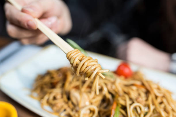 istock Woman's hand uses chopsticks to serve Thai chicken noodle dish 867704900