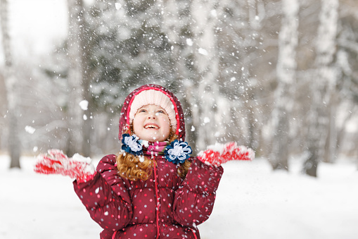 Curly hair girl catching falling snowflakes. Magic first snow.