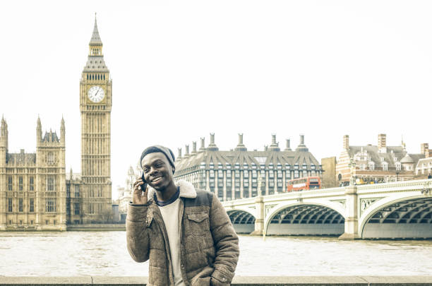 African american young man using mobile smart phone at Thames riverbank in London - Hipster guy male model with modern cell smartphone wearing trendy fashion clothes - Bright desaturated filter