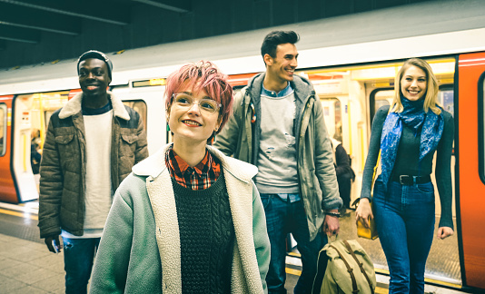 Multiracial hipster friends group walking at tube subway station - Urban friendship concept with young people having fun in city underground area - Teal and orange filter with focus on pink hair girl