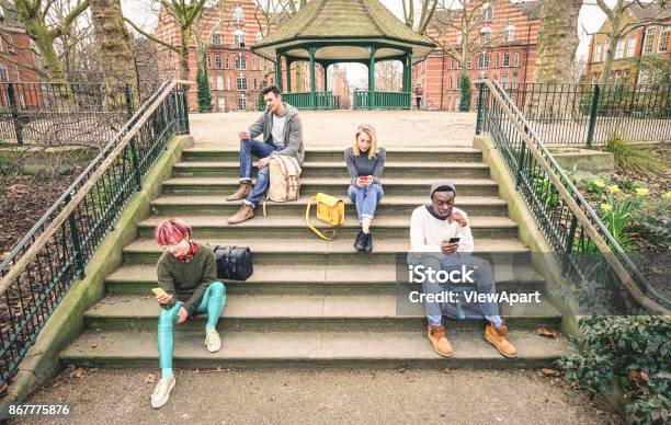Group Of Multiracial Friends Using Mobile Smart Phone Sitting On Stairs At Park Young Hipster People Addicted By Smartphone On Social Network Community Technology Concept Desaturated Color Tones Stock Photo - Download Image Now