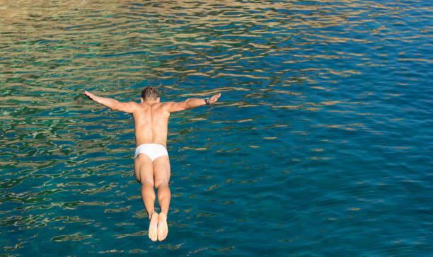 tipo de buzo acantilado saltando en el mar azul de alta rocas de pared - concepto de alegre libertad y despreocupada sensación sintiendo la conexión pura con la naturaleza - natural tonos vivos de color por la tarde - salto desde acantilado fotografías e imágenes de stock