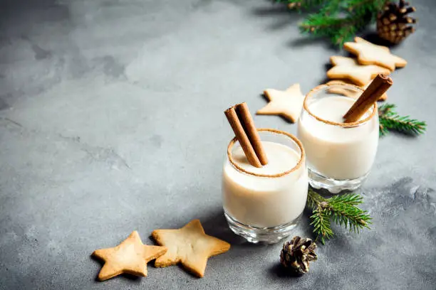 Eggnog with cinnamon and nutmeg for Christmas and winter holidays. Grey concrete background with Christmas Eggnog, gingerbread cookies, pine cones, copy space.