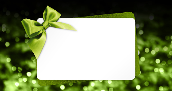 greeting gift card with green ribbon bow isolated on blurred christmas lights background and white template copy space