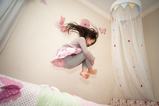 A pretty little girl is playing in her bedroom and dancing/jumping on her bed.  A great example of girl power - a blend of feminine and strength.