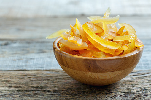 Candied orange and lemon peels in bowl on old wooden table.