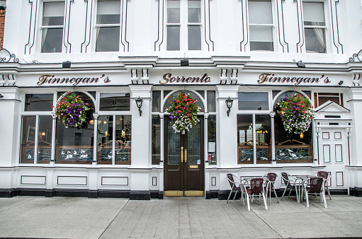 Facade of Finnegan's restaurant in Dalkey Ireland during day of autumn. There are three flower pots hanging and two small patio tables and chairs. No people