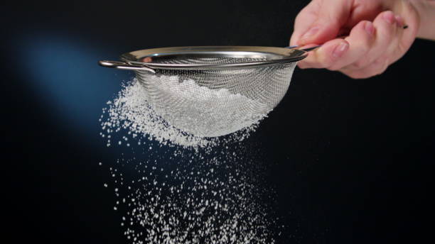 Female hand sifting flour against a dark blue background. Close-up shot