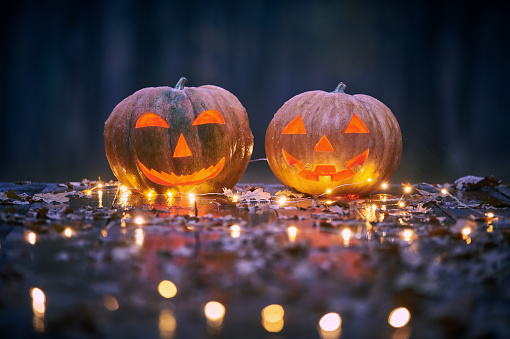 Two smiling Halloween Pumpkins on a wooden table with lights In A Mystic Forest At Night.