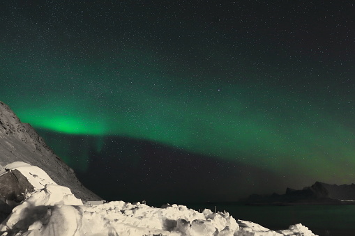 Green lights-aurora borealis illuminate from the N.mounts Ytresandheia-Roren to the E.at Yttresand village on Sandbotnen bay-N.Flakstadoya island on a cold quiet night. Lofoten-Nordland fylke-Norway.
