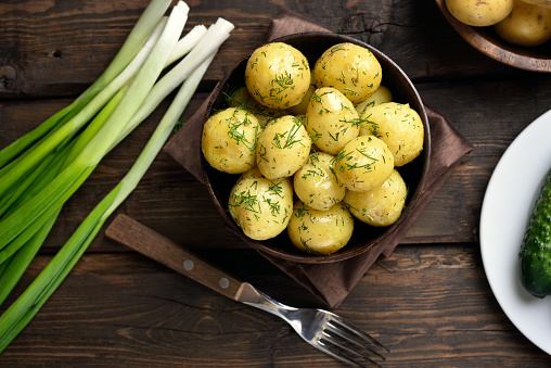 New boiled potatoes with dill in bowl on wooden background, top view