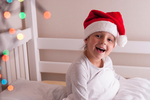cute little girl in santa hat sits on the bed