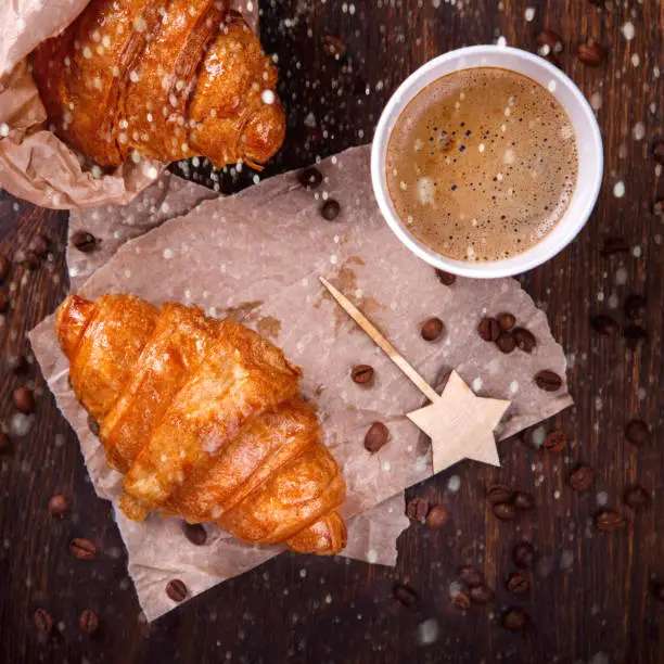 Christmas or New Year pastries,Croissant with a warming drink,coffee.Winter Holidays Concept.Holiday Decorations. top view.Toned image.Drawn Snowfal.selective focus.