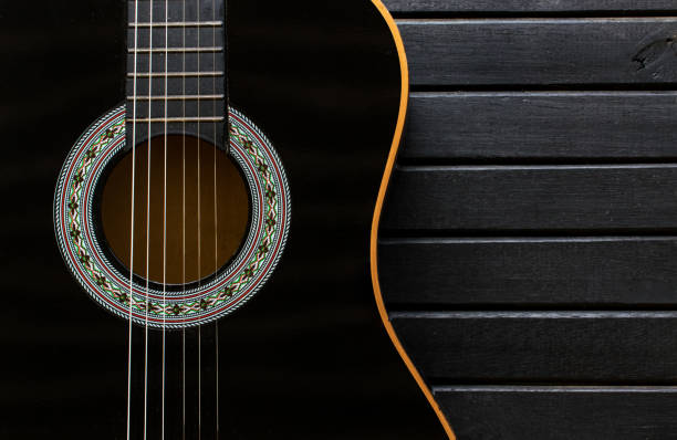 guitarra acústica negra cuerpo closeup, vertical, sobre un fondo de mesa de madera negra, con mucha textura, mostrando el espacio de la forma y la copia de guitarra - musical instrument string music dark old fashioned fotografías e imágenes de stock