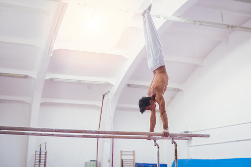 21 years old man at the gym. He is doing some exercises on parallel bars, and preparing for world championship