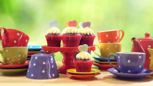 Colorful Mad Hatter style tea party with cupcakes and rainbow colored polka dot cups and saucers, with bokeh garden background and lens flare, with copy space.