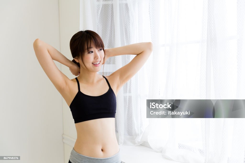 sporty asian woman relaxing in living room Sports Bra Stock Photo