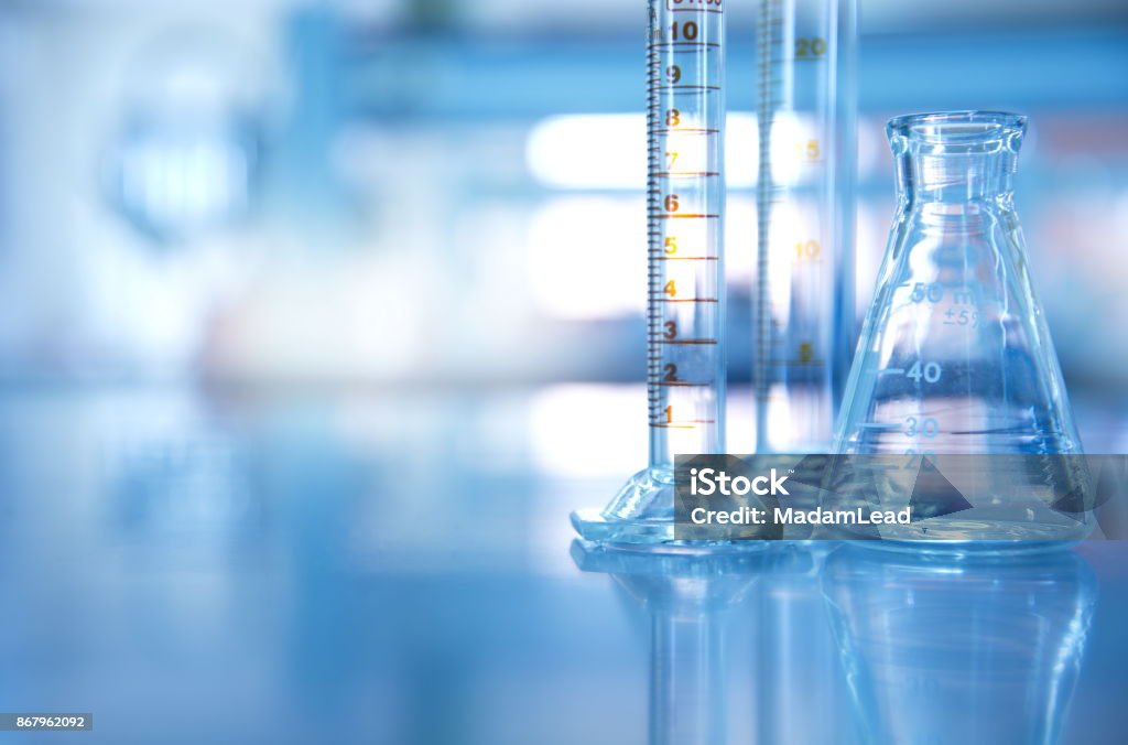 glass flask with cylinder in blue science laboratory background glass flask with measurement cylinder in blue science laboratory background Laboratory Stock Photo