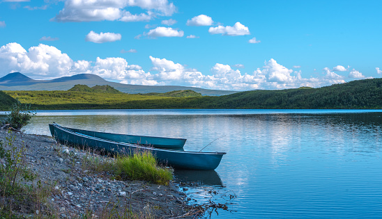 Two blue canoes on the shore of a calm lake with green hills in background