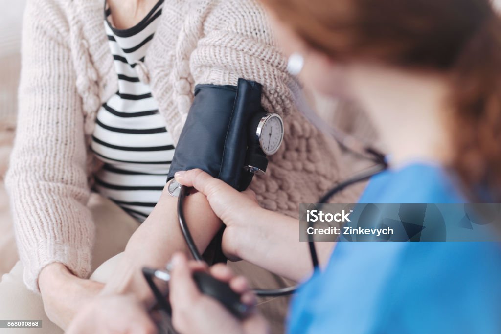 Scaled up look on nurse checking arterial pressure Less worries more positive moments. Close up view on a female nurse sitting in front of a senior patient while measuring her blood pressure during a regular visit. Blood Pressure Gauge Stock Photo