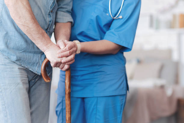 Close up of female nurse helping elderly patient to walk Support is what matters. Scaled up look on a senior man leaning on a wooden walking stick and getting help from a medical worker while trying to walk. aids walk stock pictures, royalty-free photos & images