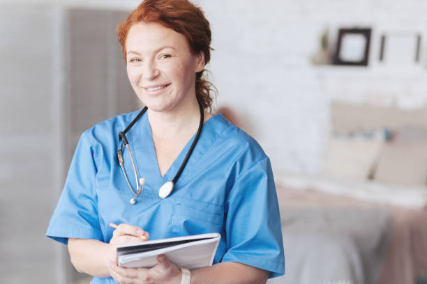 freundlich aussehende krankenschwester mit notebook lächeln in die kamera - atmungsorgan stock-fotos und bilder