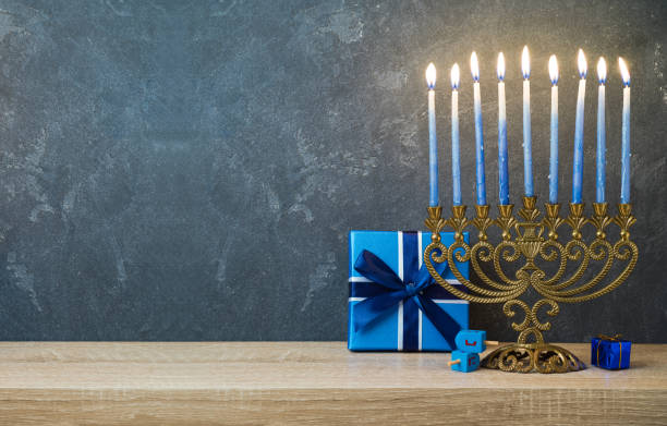 Hanukkah celebration with menorah Hanukkah celebration with menorah, gift box and dreidel on wooden table over blackboard background hanukkah candles stock pictures, royalty-free photos & images