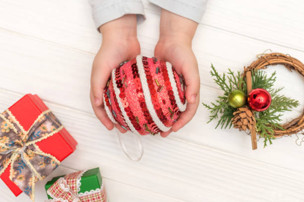 白い背景の上のクリスマス カレンダーです。子供の手が白いテーブルの上のギフト ボックスの近くのクリスマス ボールを保持 - christmas ball christmas ornament human hand ストックフォトと画像