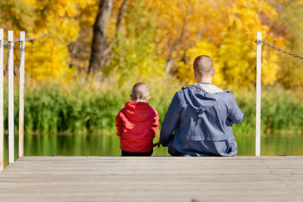 istock Father and son are sitting on the dock. Autumn, sunny. Back view 868034354