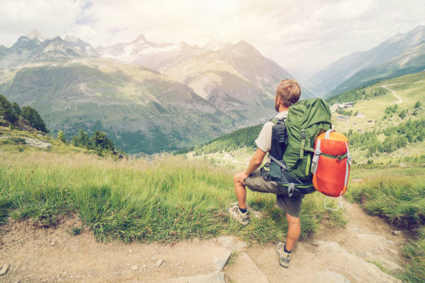 Hiker male stops on mountain trail in Zermatt with the view on the Matterhorn mountain peak. People enjoying outdoor activity concept