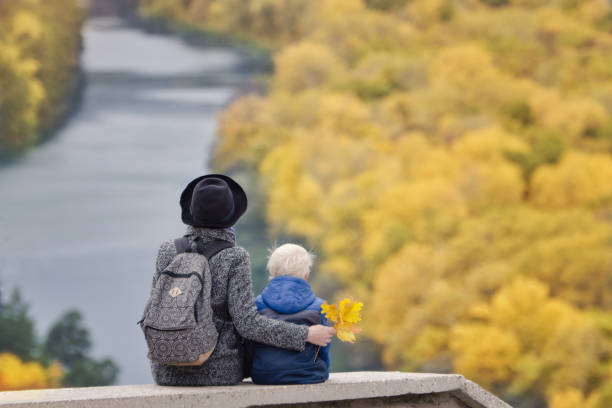 istock Mother and son are sitting on a high ground. Autumn. River and forest below. Back view 868038292