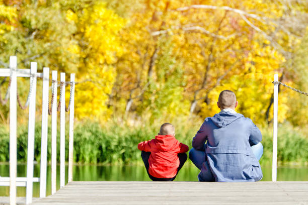 istock Father and son are sitting on the dock. Autumn, sunny. Back view 868041500