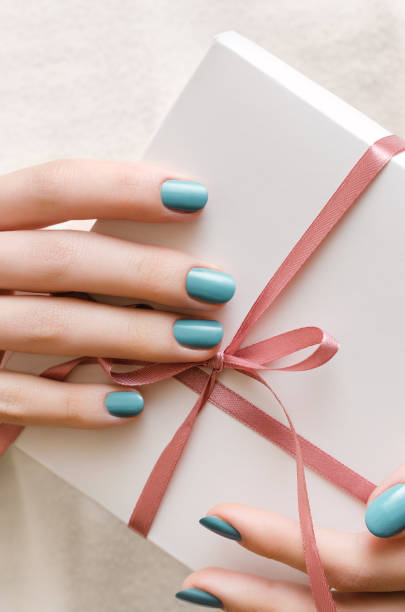 istock Female hands with turquoise manicure holding gift box. 868049026