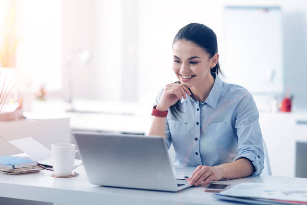 istock Beaming young lady looking at laptop and smiling at work 868054710