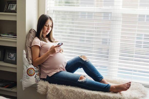 sourire de femme enceinte à l’aide de son smartphone à la maison - using computer bedroom one woman only cheerful photos et images de collection