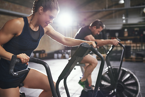 Young male and female wearing sportswear riding toughly cycling machines in light modern gym.