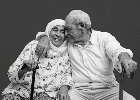 Close up portrait of an elderly couple hugging. Both of them holding a walking cane in one hand. Studio shot. Image taken with Nikon D800 and developed from Raw