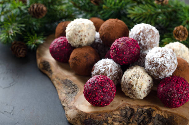 caramelle al cioccolato vegane fatte in casa con lampone essiccato, cocco grattugiato, noci, cacao su una tavola di legno fatta di ulivo e sfondo di pietra scura. rami di abete sul retro. messa a fuoco selettiva, copyspace - truffle chocolate candy chocolate candy foto e immagini stock