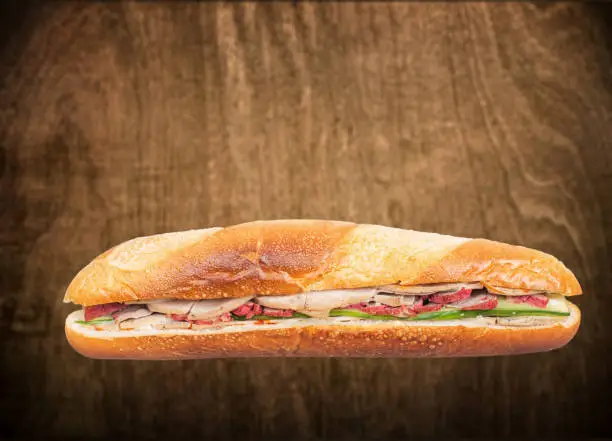 Photo of Banh Mi, Vietnamese sandwich filled with pork sausage and barbeque pork against a wooden background