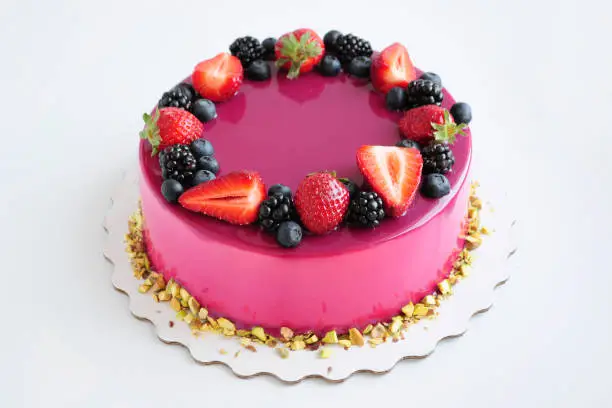 Photo of Mousse cake with pink mirror glaze, berries, pistachios.