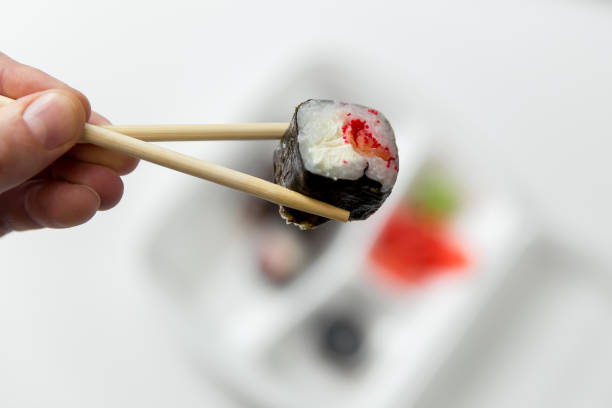 Hand takes roll. Set with chopsticks, ginger, soy sauce in container delivery