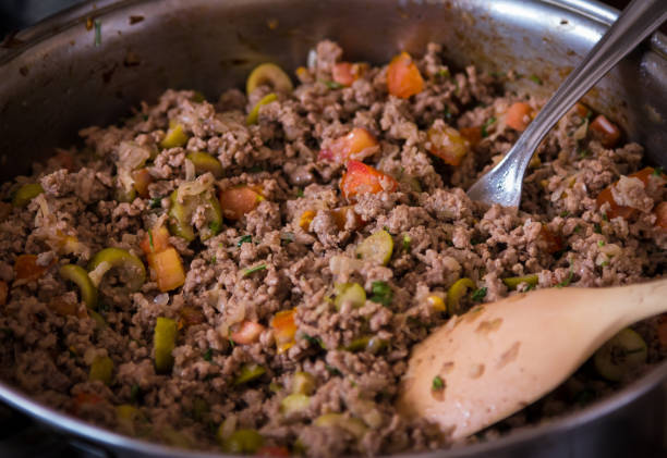 Simple but delicious ground meat frying in pan! Close up shot using selective focus of a simple but appetizing homemade braising food, ground meat with chopped tomato and olive and onion, being prepared inside a pan with cutlery braising pan stock pictures, royalty-free photos & images