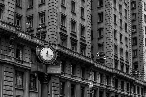 Black and white iconic old style street clock in front of buildings with windows with old street lamp posts in downtown area of São Paulo, Brazil, one of the biggest cities in the world.