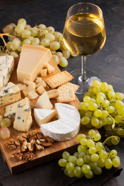istock Assorted cheeses with white grapes, walnuts, crackers and white wine on a wooden Board. Food for a romantic date on a dark stone background. Top view 868205026