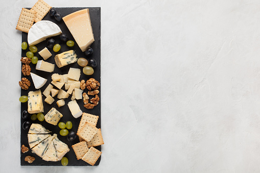 Assorted cheeses with white grapes, walnuts, crackers and on a stone Board. Food for a romantic date on a light background. Top view with copy space.