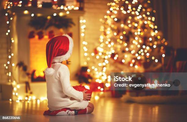 Muchacha Del Niño Sentarse Frente A Árbol De Navidad En La Nochebuena Foto de stock y más banco de imágenes de Navidad