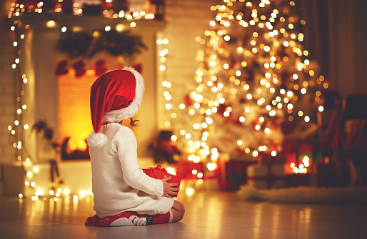 child girl is sitting with her back in front of Christmas tree on Christmas Eve