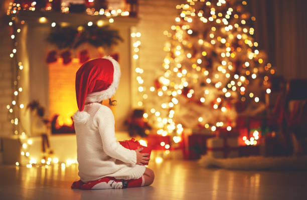 menina criança sentado em frente a árvore de natal na véspera de natal - christmas family child christmas tree - fotografias e filmes do acervo